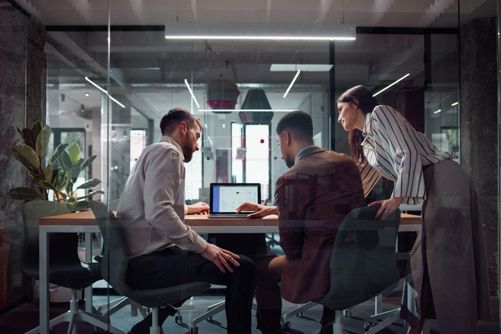 Three professionals collaborating around a laptop in a modern office: System Force IT Microsoft 365 services